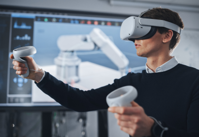 Élève ingénieur portant un casque de réalité virtuelle, tenant des manettes de jeu et contrôlant un membre bionique pendant que des actions sont affichées à l'écran